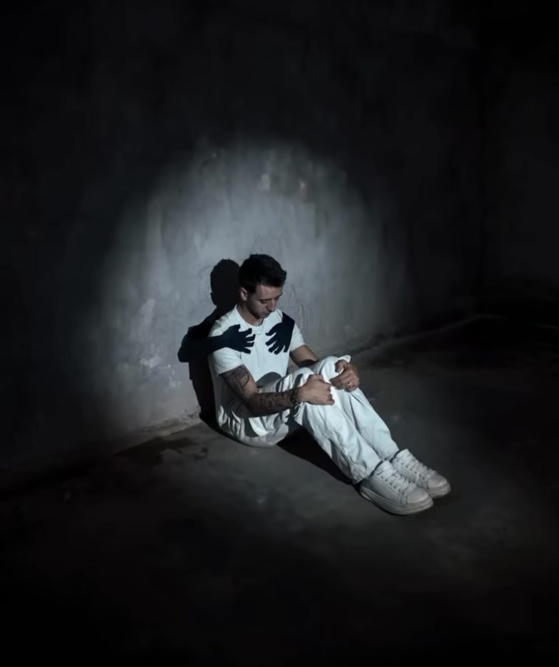 Man sitting alone in dark room with shadow hands on his chest, symbolising rumination, people-pleasing and men’s mental health struggles in Sydney